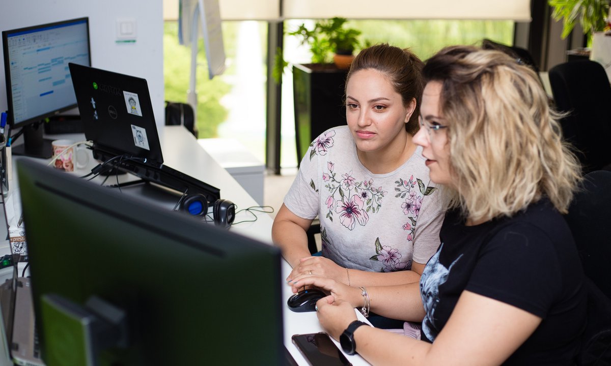 QA software tester and software developer sitting together looking at code on a desktop computer