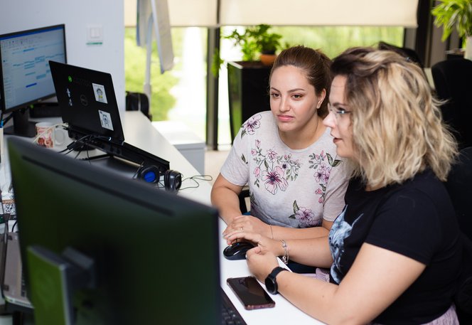 QA software tester and software developer sitting together looking at code on a desktop computer