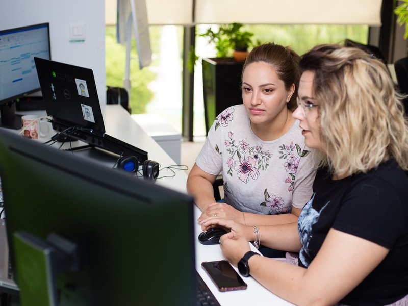 QA software tester and software developer sitting together looking at code on a desktop computer