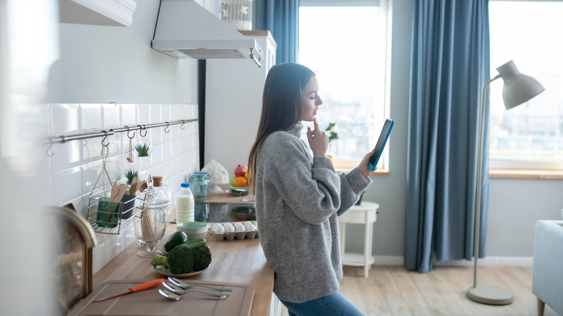 Vrouw in woonkamer denkend en kijkend naar tablet
