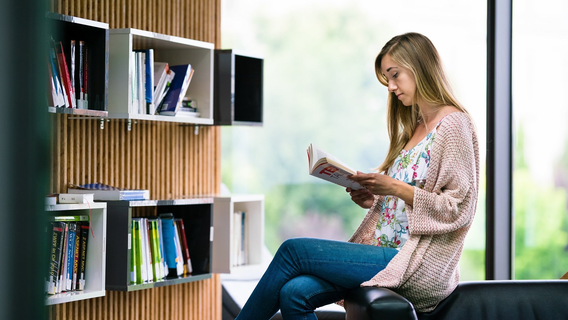 Software developer sitting in the library reading a book