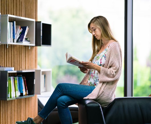 Software developer sitting in the library reading a book