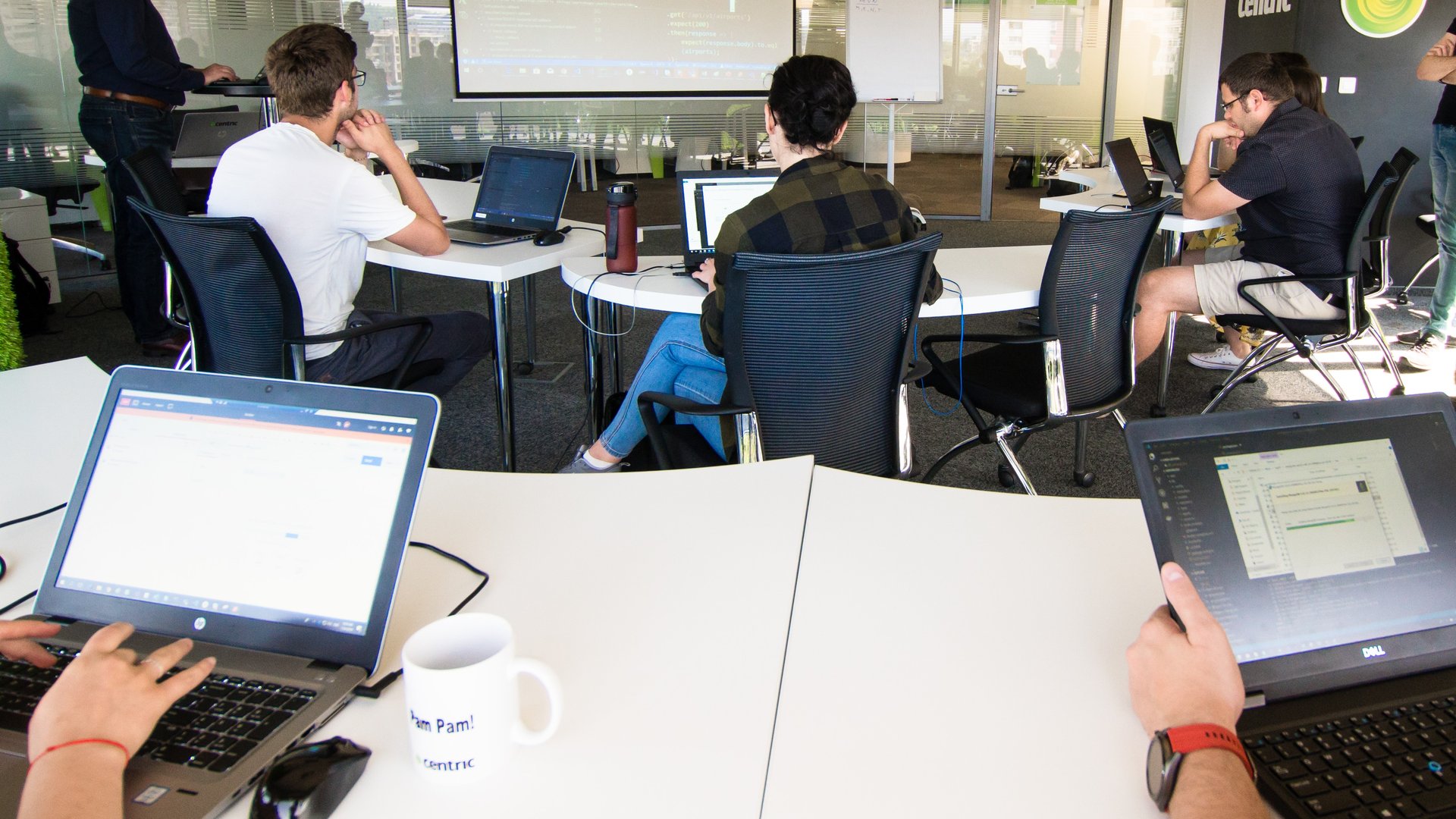 students software developers QA software testers sitting in a conference room working on laptops, listening to a trainer in a course