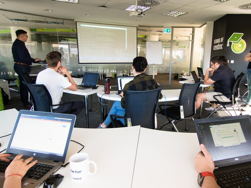 students software developers QA software testers sitting in a conference room working on laptops, listening to a trainer in a course